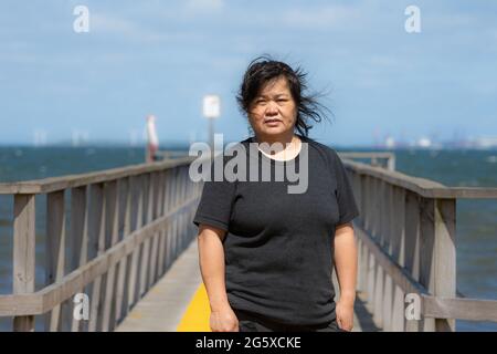 Une femme asiatique d'âge moyen sur une jetée avec un océan bleu et le ciel en arrière-plan. Photo du comté de Scania, Suède Banque D'Images