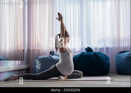 Une femme européenne enceinte fait des pilates seule. Femme enceinte au cours du dernier trimestre pratique le yoga. La fille est étirée pendant 9 mois. Banque D'Images