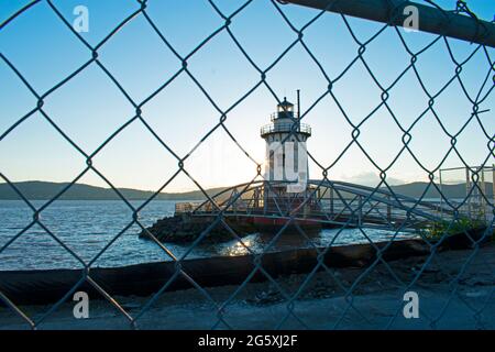 Petit phare rouge et blanc sur la rivière Hudson, vue à travers une clôture en chaînette et vers le soleil couchant -04 Banque D'Images