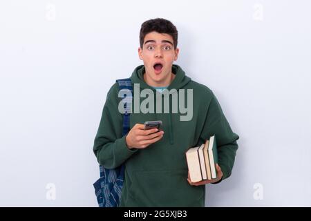 étudiant adolescent isolé avec téléphone cellulaire, livres et sac à dos avec expression surprise Banque D'Images