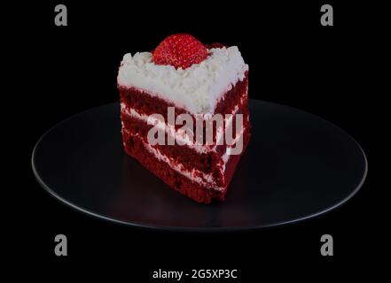 Morceau de gâteau recouvert de crème aux protéines et de fraises sur une assiette noire et un fond noir isolé Banque D'Images