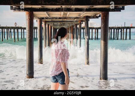 Turquie, Mer méditerranée. Une jeune femme s'est détournée de l'appareil photo, s'éloignant des vagues sous une jetée en bois. Banque D'Images