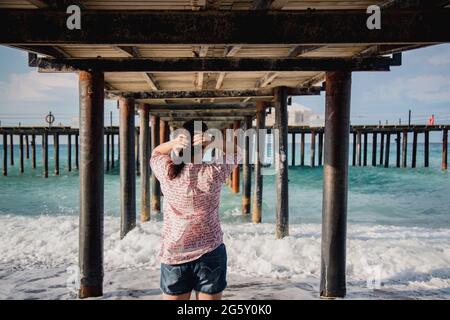 Turquie, Mer méditerranée. Une jeune femme s'est détournée de l'appareil photo, s'éloignant des vagues sous une jetée en bois. Banque D'Images