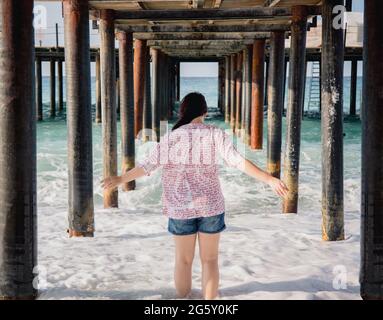 Turquie, Mer méditerranée. Une jeune femme s'est détournée de l'appareil photo, s'éloignant des vagues sous une jetée en bois. Banque D'Images