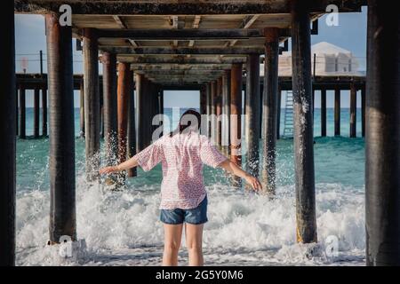 Turquie, Mer méditerranée. Une jeune femme s'est détournée de l'appareil photo, s'éloignant des vagues sous une jetée en bois. Banque D'Images