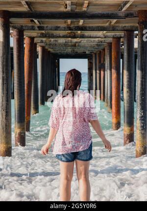 Turquie, Mer méditerranée. Une jeune femme s'est détournée de l'appareil photo, s'éloignant des vagues sous une jetée en bois. Banque D'Images
