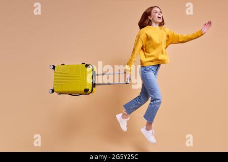 Jeune belle redhead femme va avoir des vacances de saut avec le sourire sur le visage tenant le sac de cabine jaune sur le fond isolé dans le studio, gaif Banque D'Images