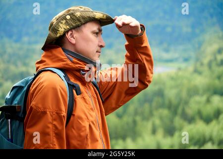 homme voyageur regarde dans la distance de sous le bras avec la toile de fond d'un paysage de montagne boisée Banque D'Images