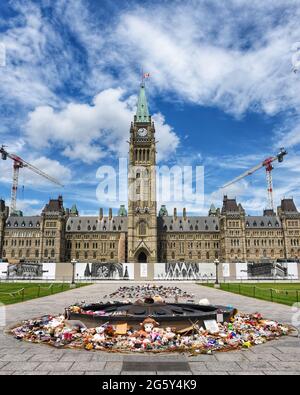 Ottawa, Canada - le 30 juin 2021 : les nombreuses chaussures et jouets laissés près de la flamme du centenaire sur la colline du Parlement à la mémoire des enfants dont les restes ont été trouvés près des anciennes pensionnats. Le drapeau canadien vole en Berne. Banque D'Images