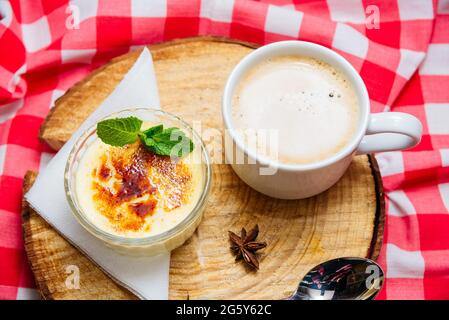 Dessert crème brûlée garni de feuilles de menthe sous forme de ramequin en verre sur une planche en bois et avec une serviette à carreaux rouge-blanc sur un côté Banque D'Images