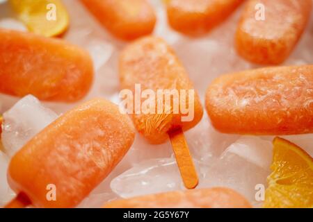 Popsicles congelés faits maison faits avec des oranges fraîches oragniques placées avec des glaçons sur une table en marbre Banque D'Images
