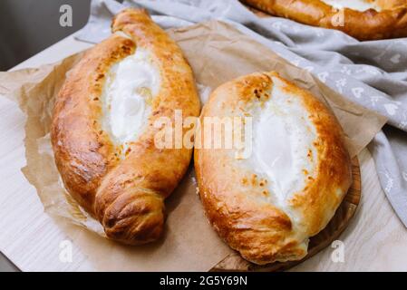 Le khachapuri chaud de style adjarien cuit avec des œufs et du fromage fondu directement du four reposent sur une planche de bois avec une serviette grise à droite Banque D'Images