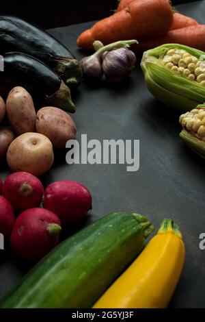 Maïs, tomates, carottes, pommes de terre, aubergines, radis et autres légumes sur une table en bois noir Banque D'Images