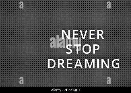 Phrase Never Stop Dreaming orthographié avec des lettres blanches sur un panneau perforé gris Banque D'Images