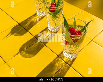 Boissons rafraîchissantes d'été dans des verres en cristal avec des feuilles vertes framboise jaune carreaux ombres de fond. Cocktail naturel doux et froid chaud en été. Donc Banque D'Images