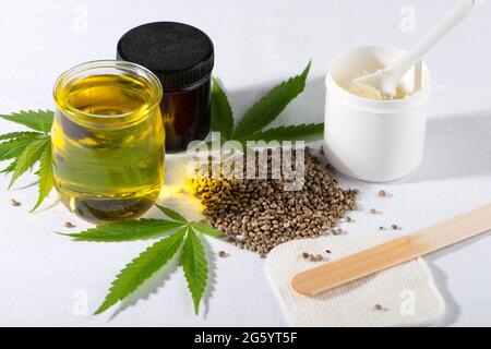 Graines de cannabis, jeunes feuilles de chanvre, huile de CBD et beurre de cannabis sur fond blanc. Pour les cosmétiques, le traitement, la thérapie. Prise de vue en grand angle. Banque D'Images