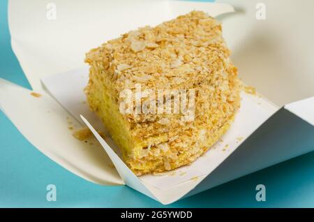 Le gâteau est emballé dans une boîte en papier blanc sur fond bleu clair. Ouvrir l'emballage Kraft avec un morceau de gâteau doux couche. Boîte à lunch écologique. F Banque D'Images