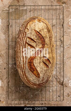 Plan plat avec vue sur le pain de levain artisanal sur une surface de travail en marbre brun clair. Fraîchement cuit sur la grille de refroidissement. Banque D'Images