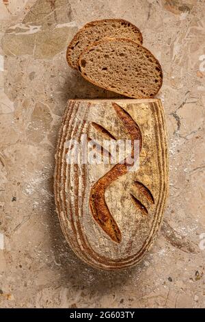 Plan plat avec vue sur le pain de levain artisanal sur une surface de travail en marbre brun clair. Fraîchement cuit et coupé en tranches. Banque D'Images