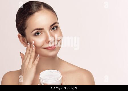 Soins de la peau. Femme appliquant de la crème faciale sur le visage de beauté gros plan. Modèle de fille souriante avec maquillage naturel en utilisant hydratant, produit cosmétique Banque D'Images