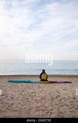 vue arrière d'un jeune garçon avec son sac d'école assis sur un bois peint dérivant, qui donne sur la mer Banque D'Images