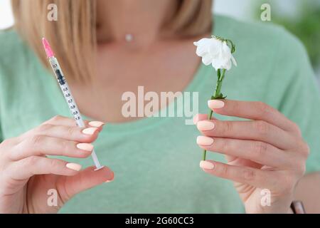 Femme esthéticienne tenant la seringue avec le médicament et la fleur flétritie dans ses mains de près Banque D'Images