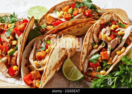 tacos avec viande de poulet grillée, maïs, cubes de patates douces rôties, poivron rouge et persil servis sur une planche de bois, gros plan Banque D'Images