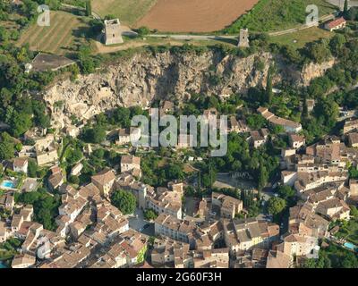 VUE AÉRIENNE. Deux tours médiévales se tenant au sommet d'une falaise au-dessus d'un vieux village et quelques maisons de falaises. Cotignac. Var, France. Banque D'Images