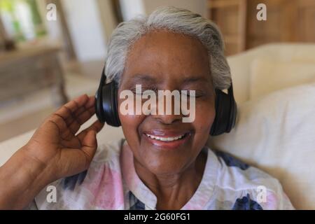 Femme afro-américaine assise sur un canapé, portant un casque avec les yeux fermés Banque D'Images