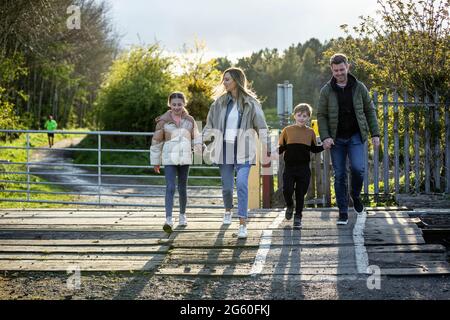 Vue de face d'une mère et d'un père caucasiens marchant avec leur fils et leur fille, ils se tiennent les mains et sourient tout en marchant au-delà d'un niveau c. Banque D'Images