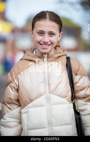 Portrait en vue de face d'une jeune fille caucasienne portant un uniforme et un manteau d'école, elle sourit et regarde l'appareil photo. Banque D'Images