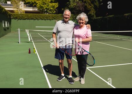 Portrait d'un couple caucasien âgé regardant l'appareil photo et souriant sur un court de tennis Banque D'Images