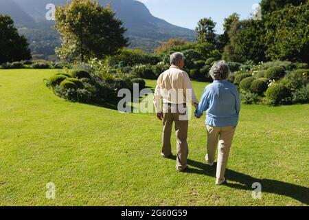 Couple caucasien senior marchant ensemble dans un jardin ensoleillé Banque D'Images