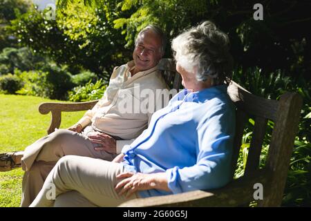 Couple caucasien senior assis sur un banc ensemble dans un jardin ensoleillé Banque D'Images
