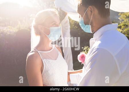 Bonne mariée caucasienne et marié se marient en portant des masques et en tenant les mains Banque D'Images