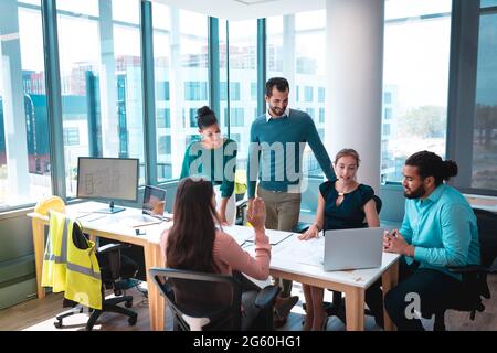 Groupe de professionnels divers discutant ensemble assis à table et utilisant un ordinateur portable Banque D'Images