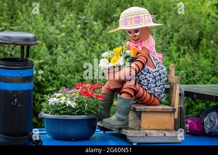 Gros plan d'une femme composée de pots de fleurs assis sur un siège en bois tenant un pot de fleurs au-dessus d'un bateau de canal. Banque D'Images