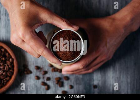 vue en grand angle d'un jeune homme caucasien insérant l'entonnoir plein de café moulu dans la marmite de moka, placée sur une table en bois rustique gris Banque D'Images
