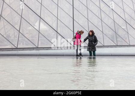 Mère équilibrant sa fille sur le bord d'un plan d'eau. Pyramide du Louvre, Paris, France Banque D'Images