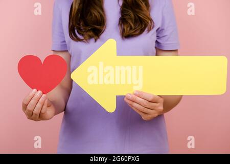 Gros plan de la jeune femelle méconnaissable tient peu de coeur rouge et de flèche jaune, isolé sur fond rose. Comme blogging blog Banque D'Images