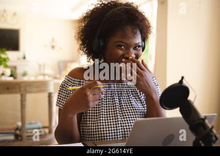 Bonne femme afro-américaine portant un casque et utilisant un micro, en riant pendant le podcast Banque D'Images