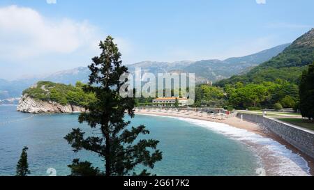 Plage vide avec chaises longues, parasols sur la toile de fond des montagnes. Mer calme, beau ciel nuageux. Au premier plan se trouvent les branches de l'arborescence. Banque D'Images