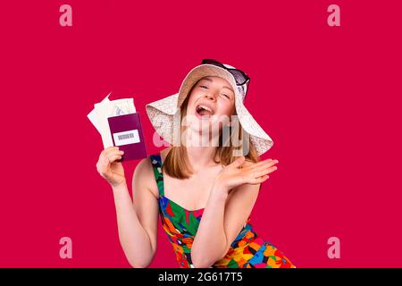 Une heureuse touriste portant un chapeau et des lunettes de soleil tenant dans la main un passeport de vaccination pour voyager. Banque D'Images