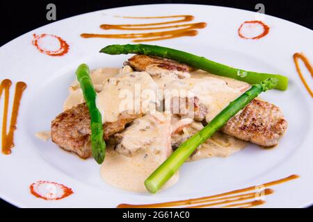 Médaillons de porc aux asperges : filet de porc, asperges, champignons, poireaux, oignons, carottes et sauce demi-glace. Banque D'Images