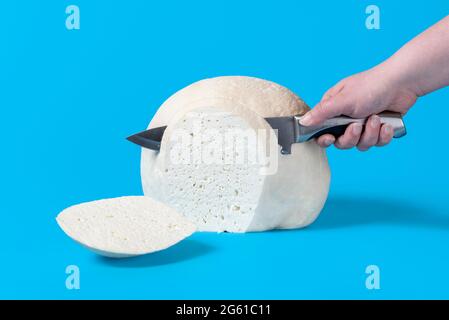 Femme trancheuse à la main à partir d'un gros bloc de fromage. Morceau de fromage roumain isolé sur fond bleu. Banque D'Images