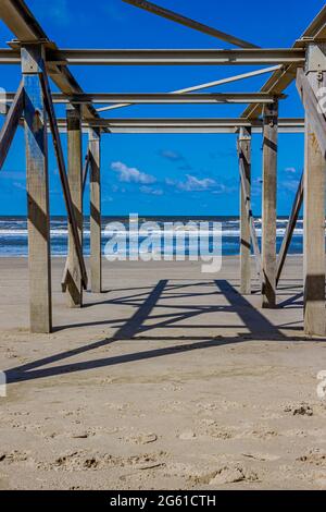 Poteaux en bois d'une structure abandonnée sur la plage avec la mer avec de petites vagues et de la mousse en arrière-plan, jour ensoleillé à Camperduin, Hollande-du-Nord i Banque D'Images