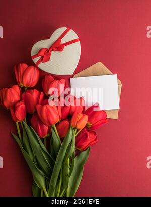 Bouquet de tulipes rouges et boîte cadeau de coeur isolée sur fond rouge . Fleurs de printemps. Carte de voeux pour anniversaire, femme, Fête des mères, mariage, Valen Banque D'Images