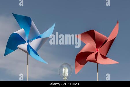 Deux pignons en papier coloré et une ampoule allumée, font le concept de l'énergie propre du vent, contre le ciel bleu Banque D'Images