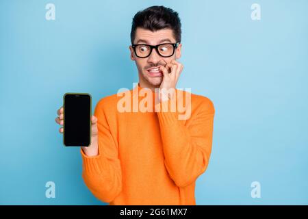 Portrait de la personne horrifiée mordant doigt tenir le téléphone montre l'affichage isolé sur fond bleu de couleur Banque D'Images