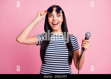 Photo portrait d'une femme choquée soulevant des lunettes tenant un microphone dans une main isolé sur fond rose pastel Banque D'Images